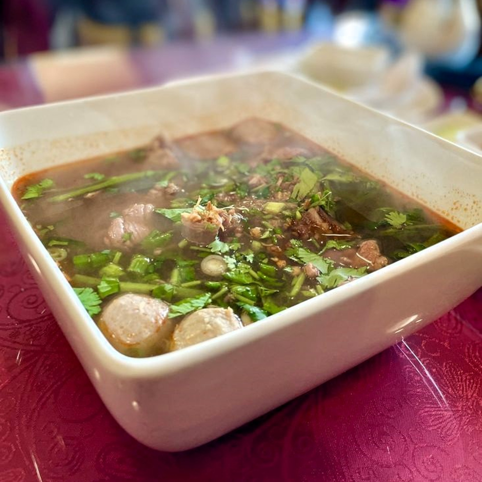 Steaming Cambodian beef noodle soup with meatballs and fresh herbs in a white bowl.