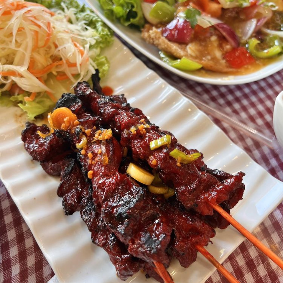 Cambodian beef skewers with a side of shredded cabbage salad and another dish in the background.