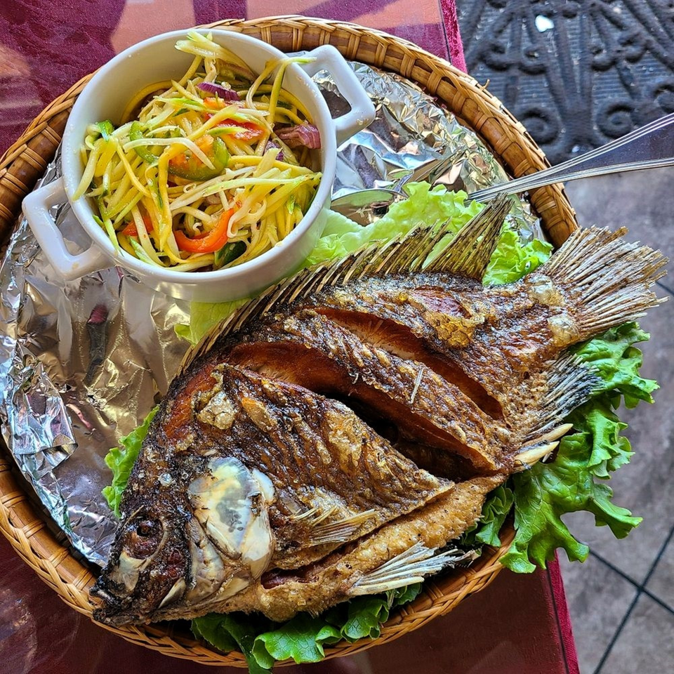 A whole fried fish with mango salad and lettuce on a woven platter at Monorom Cambodian Restaurant.