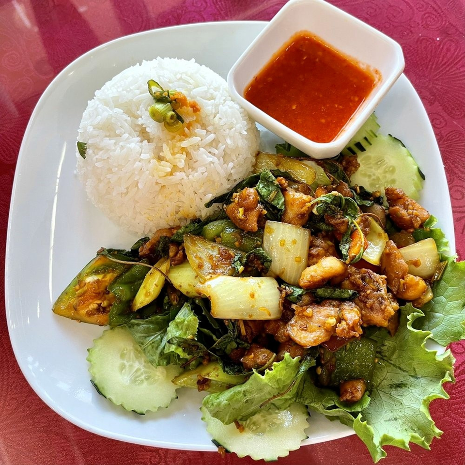 Cambodian stir-fried chicken with vegetables and rice, served with a side of chili sauce.