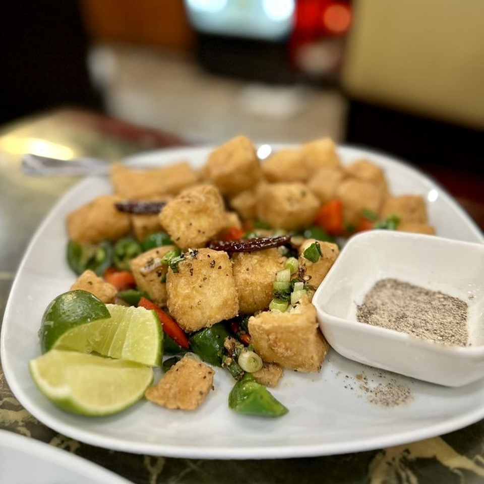 Crispy fried tofu with green onions, red peppers, and lime wedges, served with a side of pepper.