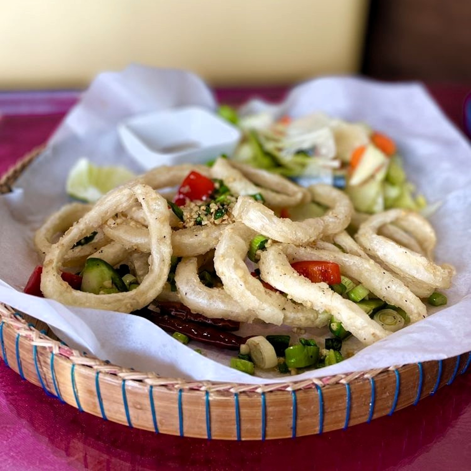 Crispy fried calamari rings with red peppers, green onions, and a side salad in a woven basket.